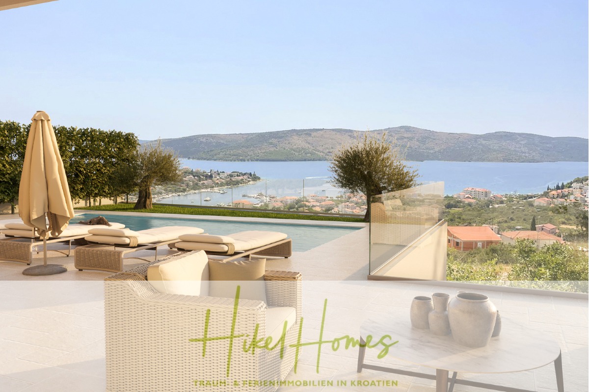 Luxuriöse Außenterrasse mit Liegestühlen, Sonnenschirm und Pool mit Blick auf eine malerische Küstenlandschaft mit Hügeln, blauem Wasser und Dächern. Dekorative Vasen stehen auf einem Tisch im Vordergrund. Text "Hikel Homes" am unteren Rand. - Meerblick – Schlüsselfertige Villa Princ in Seget Vranijca – modernste Technik – 3 SZ