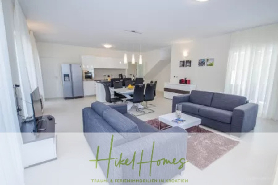 Villa im Mittelmeerstil mit 3 SZ, Pool, Dachterrasse mit Meerblick (2) - Moderner, heller, offener Wohn- und Essbereich mit zwei grauen Sofas, einem Esstisch mit schwarzen Stühlen, einer Küche mit weißen Schränken und Edelstahlgeräten sowie großen Fenstern mit transparenten Vorhängen. (45792)