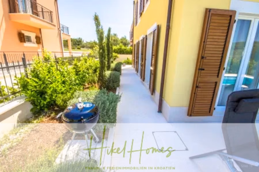 Villa im Mittelmeerstil mit 3 SZ, Pool, Dachterrasse mit Meerblick (2) - Eine sonnige Terrasse mit einer gelben Fassade und Holzfensterläden. Im Gartenbereich, umgeben von üppigen grünen Pflanzen, befindet sich ein kleiner runder Grill. Ein Liegestuhl ist auf der Terrasse teilweise sichtbar. (42191)