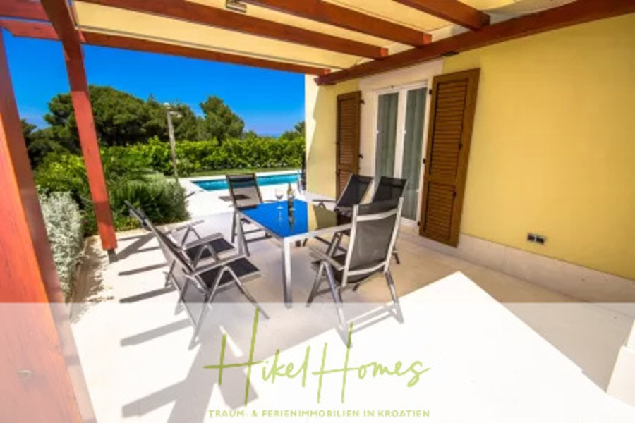 Villa im Mittelmeerstil mit 3 SZ, Pool, Dachterrasse mit Meerblick (2) - Eine überdachte Terrasse mit einem Esstisch aus Glas und sechs Stühlen bietet an sonnigen Tagen einen Blick auf den Pool und das üppige Grün. Das Haus hat gelbe Wände, braune Fensterläden und Schiebetüren. Das Logo von "Hikel Homes" befindet sich am unteren Rand. (45781)