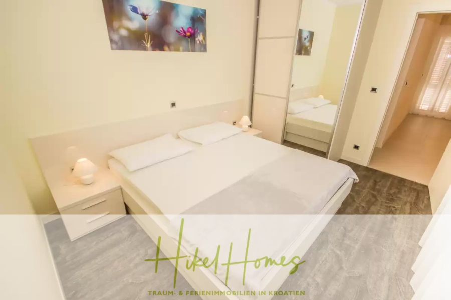 Villa im Mittelmeerstil mit 3 SZ, Pool, Dachterrasse mit Meerblick (2) - Ein helles Schlafzimmer mit einem großen Doppelbett, zwei weißen Nachttischen, einem verspiegelten Kleiderschrank und einer modernen Einrichtung. Über dem Bett hängt ein Kunstwerk, und durch eine offene Tür fällt Sonnenlicht herein. Der Text "Hikel Homes" ist unten eingeblendet. (45799)