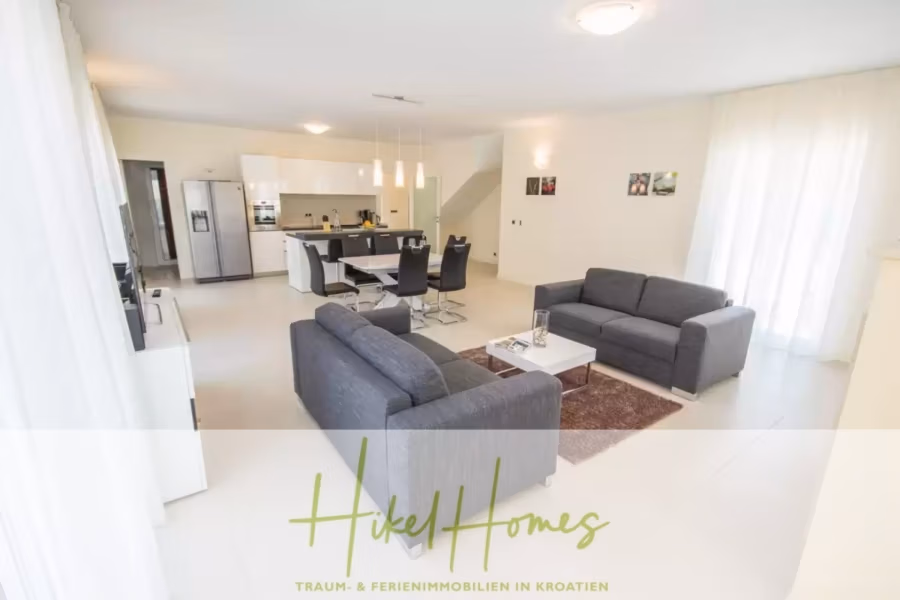 Villa im Mittelmeerstil mit 3 SZ, Pool, Dachterrasse mit Meerblick (1) - Großzügiger, moderner Wohnbereich mit grauen Sofas, einem quadratischen Couchtisch und einem Teppich. Die angrenzende offene Küche ist mit weißen Schränken, schwarzen Esszimmerstühlen und einem Tisch ausgestattet. Helles Interieur mit großen Fenstern und minimalistischem Dekor. (40953)