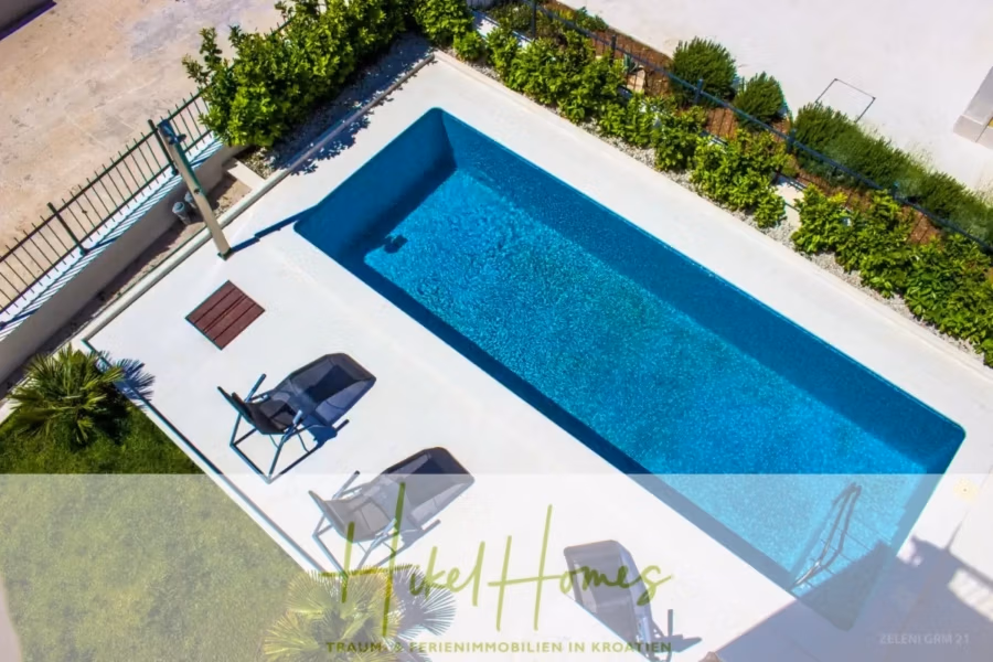 Villa im Mittelmeerstil mit 3 SZ, Pool, Dachterrasse mit Meerblick (1) - Draufsicht auf einen rechteckigen Swimmingpool, umgeben von Grün. Zwei Liegestühle mit Handtüchern stehen seitlich am Pool. Daneben steht ein kleiner Holztisch. Der Poolbereich ist eingezäunt. (40947)