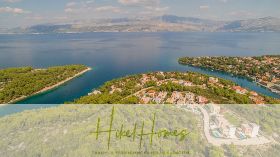Villa im Mittelmeerstil mit 3 SZ, Pool, Dachterrasse mit Meerblick (1) - Luftaufnahme einer Küstenstadt in Kroatien mit üppigen grünen Wäldern, blauem Meer und verstreuten Häusern. Das Logo von Hikel Homes und der deutsche Text überlagern sich am unteren Rand. Im fernen Hintergrund sind unter einem teilweise bewölkten Himmel Berge zu sehen. (44778)