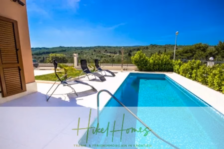 Villa im Mittelmeerstil mit 3 SZ, Pool, Dachterrasse mit Meerblick (1) - Blick vom Dach auf einen modernen Swimmingpool mit Liegestühlen unter strahlend blauem Himmel. Üppiges Grün umgibt den Poolbereich, im Hintergrund Hügel. Ein Markentext überlagert die Botschaft „Hikel Homes“. (40948)