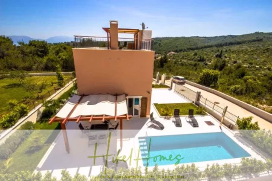 Villa im Mittelmeerstil mit 3 SZ, Pool, Dachterrasse mit Meerblick (1) - Eine moderne zweistöckige Villa mit Pool und Pergola, umgeben von Grün und mit Blick auf die Berge in der Ferne. Der Himmel ist strahlend blau, und in der Nähe der Einfahrt parkt ein Auto. Das Logo „Hikel Homes“ befindet sich am unteren Bildrand. (40952)