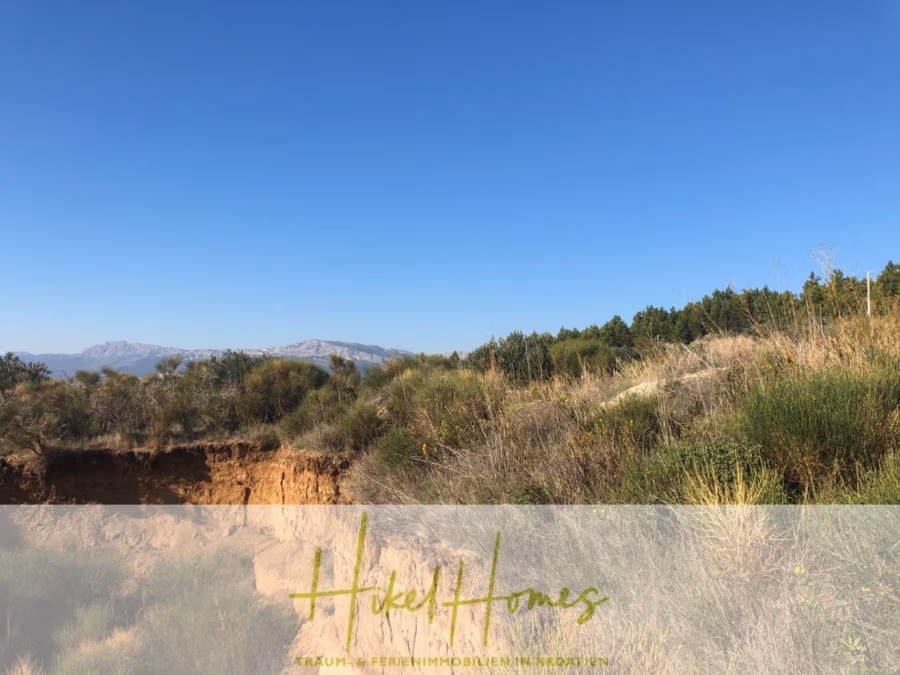 Absolute Alleinlage mit Blick auf Meer, Insel Brac und Split – 511m² auf über 3100m² Grundstück - Eine malerische Landschaft mit klarem, blauem Himmel, fernen Bergen und dichtem Grün mit Sträuchern und Gras. Das Gelände umfasst eine kleine Klippe und wirkt natürlich und unberührt. Unten steht halbtransparent „Hikel Homes“. (43249)