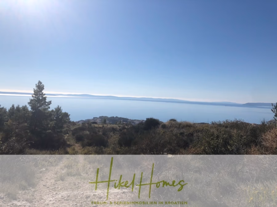 Absolute Alleinlage mit Blick auf Meer, Insel Brac und Split – 511m² auf über 3100m² Grundstück - Ein malerischer Blick auf eine Küste mit klarem, blauem Himmel, fernen Bergen und einem weitläufigen Meer. Kiefern und Büsche im Vordergrund rahmen die ruhige Landschaft ein. Der Text unten lautet: „Hikel Homes, Bau & Ferienimmobilien in Kroatien.“. (43237)