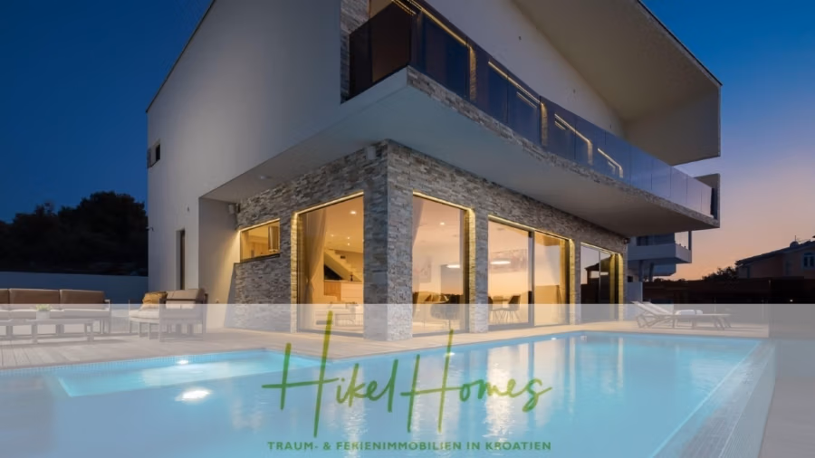 Bezugsfertige Luxus-Meerblick Villa mit 4 SZ, Pool, Sauna, Fitness, Jacuzzi, vollständig möbliert - Modernes, zweistöckiges Haus mit großen Fenstern und einem Pool davor. Die untere Etage ist beleuchtet und spiegelt sich in der Pooloberfläche. Der Text lautet: „Hikel Homes – Traum- & Ferienimmobilien in Kroatien“. Im Hintergrund der Abendhimmel. (42246)