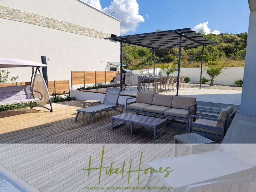 Bezugsfertige Luxus-Meerblick Villa mit 4 SZ, Pool, Sauna, Fitness, Jacuzzi, vollständig möbliert - Moderne Außenterrasse mit Holzbelag und Loungebereich mit Sofas, Stühlen und Schaukel. Eine Pergola spendet Schatten über einem Barbereich mit Hockern. Die Umgebung besticht durch üppiges Grün und eine weiße Gebäudekulisse. (42255)