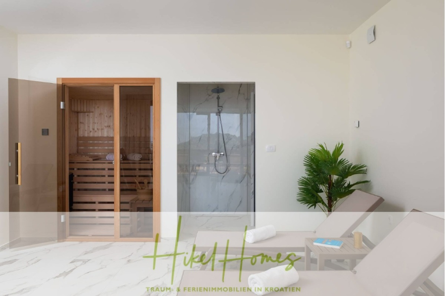 Bezugsfertige Luxus-Meerblick Villa mit 4 SZ, Pool, Sauna, Fitness, Jacuzzi, vollständig möbliert - Moderner Spa-Raum mit einer Holzsauna auf der linken Seite, einer Dusche mit Glastür in der Mitte, zwei beigen Liegestühlen, einem kleinen Tisch mit Handtüchern und Wasser und einer Topfpalme auf der rechten Seite. (45642)