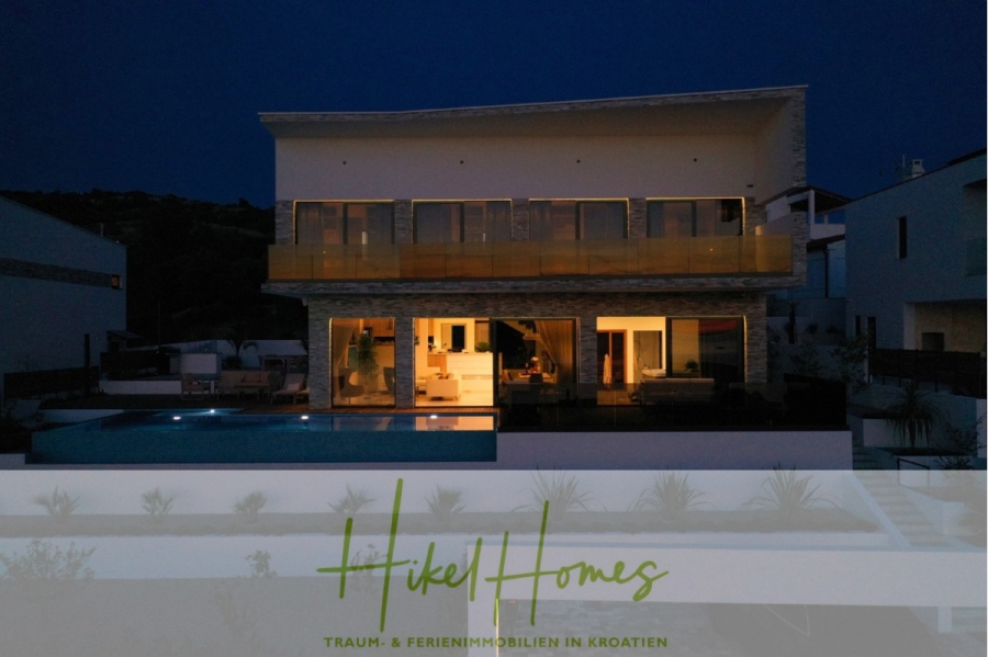 Bezugsfertige Luxus-Meerblick Villa mit 4 SZ, Pool, Sauna, Fitness, Jacuzzi, vollständig möbliert - Moderne zweistöckige Villa mit großen Fenstern und einem Pool, nachts beleuchtet. Das Logo "Hikel Homes" und der Text "TRAUM- & FERIENIMMOBILIEN IN KROATIEN" erscheinen am unteren Rand des Bildes. (45650)