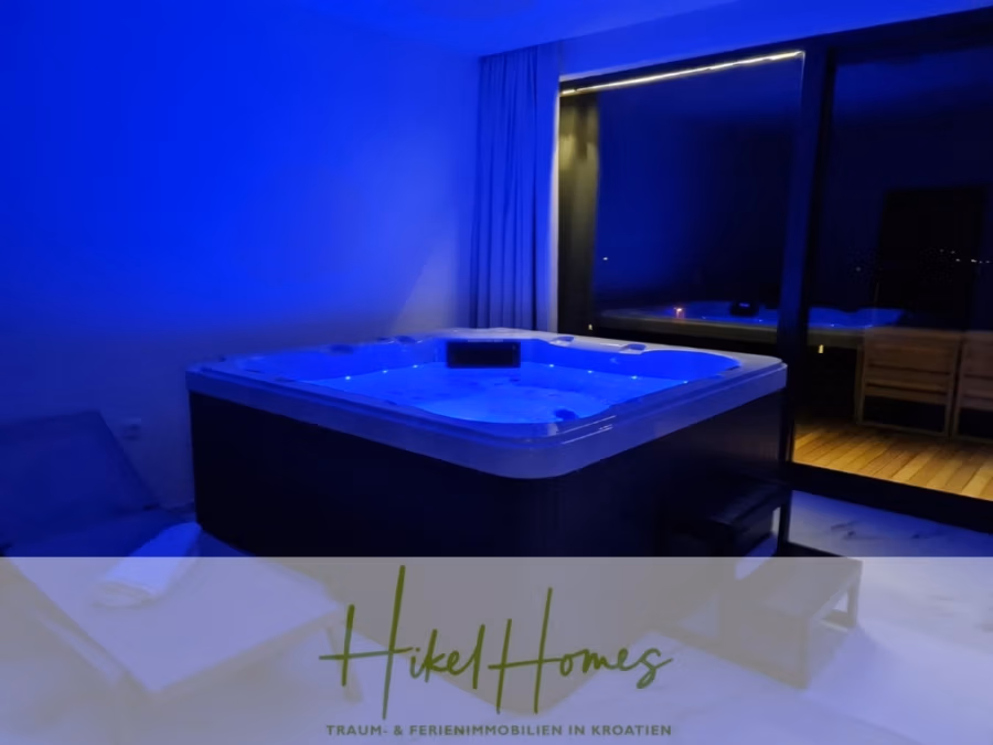 Bezugsfertige Luxus-Meerblick Villa mit 4 SZ, Pool, Sauna, Fitness, Jacuzzi, vollständig möbliert - Ein schwach beleuchteter Raum mit einem blau getönten Whirlpool. Große Fenster bieten einen nächtlichen Blick nach draußen und eine kleine Sauna ist sichtbar. In der Ecke stehen ein Liegestuhl und gefaltete Handtücher. Das Logo unten lautet „Hikel Homes: Traum- & Ferienimmobilien in Kroatien“. (42262)