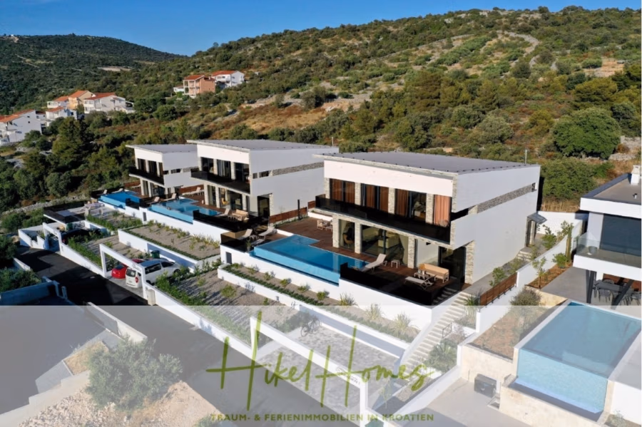 Bezugsfertige Luxus-Meerblick Villa mit 4 SZ, Pool, Sauna, Fitness, Jacuzzi, vollständig möbliert - Luftaufnahme eines modernen Wohnkomplexes am Hang mit drei großen, weißen Häusern mit privaten Pools und Terrassen. Umgeben von Grünflächen und anderen Häusern bietet der Komplex eine malerische Landschaft. Der Logotext unten lautet „HikeHomes“. (42251)