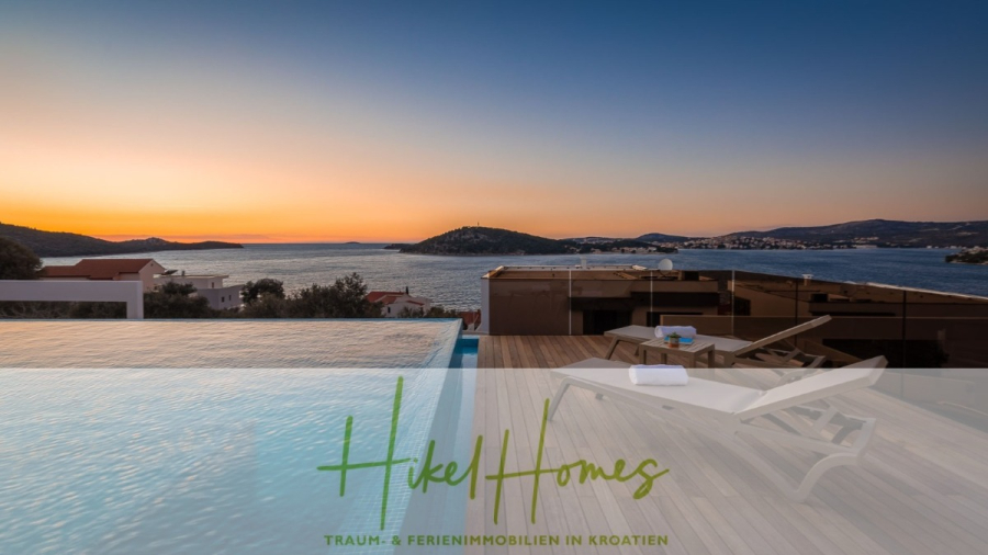 Bezugsfertige Luxus-Meerblick Villa mit 4 SZ, Pool, Sauna, Fitness, Jacuzzi, vollständig möbliert - Der Infinity-Pool und die Liegestühle auf dem Holzdeck bieten einen Blick auf das Meer und die fernen Hügel bei Sonnenuntergang. Der Himmel ist orange und blau. Das Bild ist mit dem Text "Hikel Homes - Traum- & Ferienimmobilien in Kroatien." überlagert. (45626)