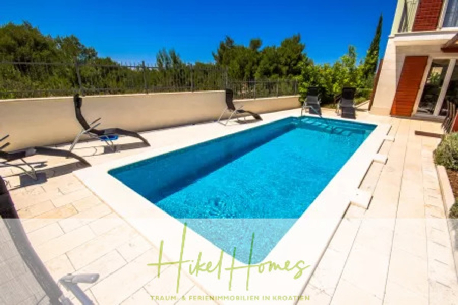 Villa im Mittelmeerstil mit 3 SZ, Pool, Dachterrasse mit Meerblick – möbiliert (15) - Ein rechteckiger Außenpool mit klarem, blauem Wasser, umgeben von Liegestühlen und einer Steinterrasse. Der Pool befindet sich neben einem modernen Haus und bietet einen Blick auf die grüne Landschaft unter einem hellen, sonnigen Himmel. (45693)