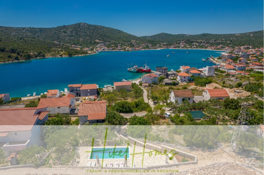 Meerblick Appartementhaus mit 3 Wohnungen, Karten, Terrassen - Luftaufnahme einer kroatischen Küstenstadt mit roten Dächern, einer blauen Bucht mit Booten und grünen Hügeln im Hintergrund unter einem klaren blauen Himmel. Der Text "HikeHomes" erscheint am unteren Rand des Bildes. (45304)