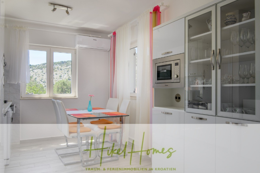 Meerblick Appartementhaus mit 3 Wohnungen, Karten, Terrassen - Helle Küche und Essbereich mit einem Glastisch für vier Personen, weißen Schränken, eingebauter Mikrowelle, großem Fenster mit Blick auf die Berge und transparenten Vorhängen, die das Sonnenlicht in den Raum lassen. (45329)