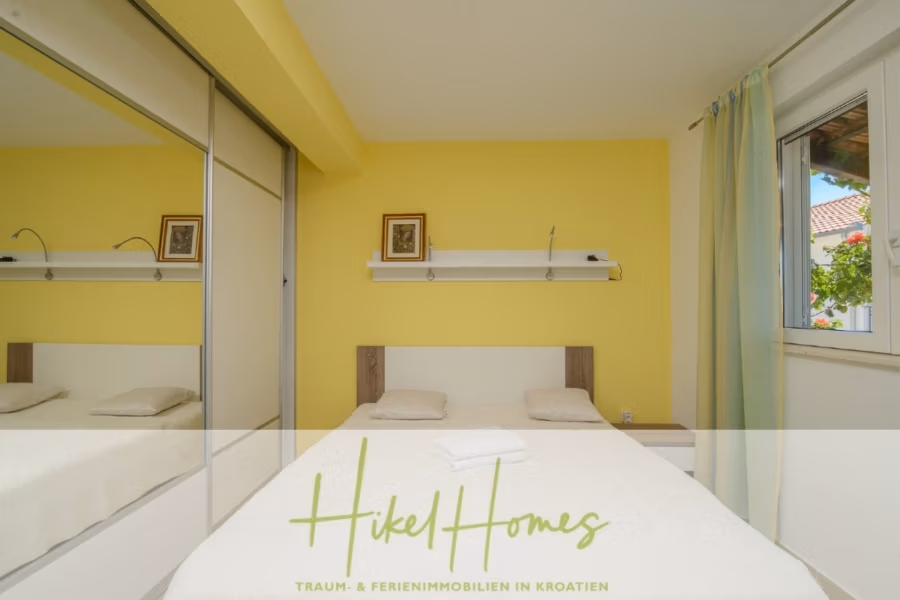 Meerblick Appartementhaus mit 3 Wohnungen, Karten, Terrassen - Einfaches Schlafzimmer mit Doppelbett, Spiegelschrank und kleinem Fenster mit hellen Vorhängen. Die Wände sind gelb, über dem Bett befindet sich ein Regal mit kleinen Gemälden, auf dem Bett liegt ein gefaltetes Handtuch. (40989)
