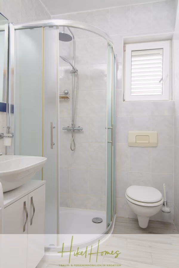 Meerblick Appartementhaus mit 3 Wohnungen, Karten, Terrassen - Kleines Badezimmer mit Glasduschkabine, weißem Waschbecken mit Unterschrank, Wandtoilette und Fenster mit Fensterläden. Wände und Boden sind mit hellen Fliesen ausgelegt, was für ein klares und minimalistisches Erscheinungsbild sorgt. (41005)