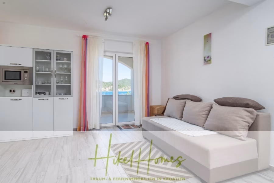 Meerblick Appartementhaus mit 3 Wohnungen, Karten, Terrassen - Helles, modernes Wohnzimmer mit hellem Sofa, farbenfrohen Vorhängen und Blick durch Glastüren auf den Balkon. Das Zimmer verfügt über weiße Schränke mit eingebautem Backofen. Zur Dekoration gehören ein Wandgemälde und eine kleine Leuchte. (40999)