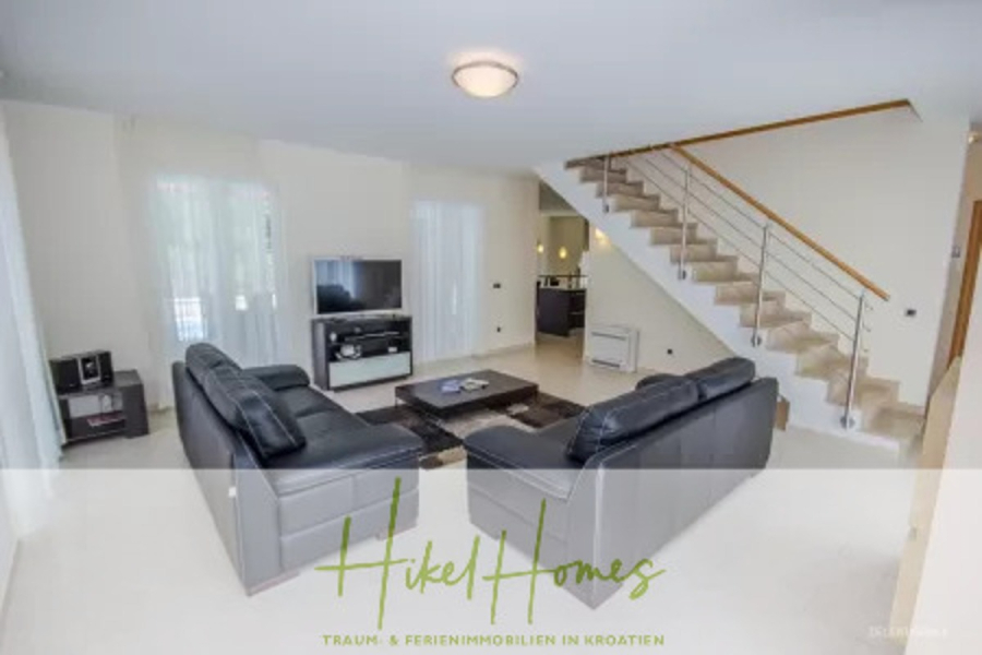 Villa im Mittelmeerstil mit 3 SZ, Pool, Dachterrasse mit Meerblick – möbiliert (9) - Modernes Wohnzimmer mit schwarzen Ledersofas, einem Couchtisch aus Glas, TV und hellem Fliesenboden. Eine Treppe mit einem Metallgeländer führt nach oben; große Fenster lassen natürliches Licht herein. Das Logo "Hikel Homes" erscheint quer über den Boden. (45721)