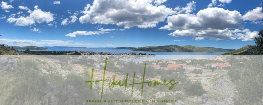 Majestätische Villa Kraljica mit Gästehaus: 610m² Luxuswohnfläche mit atemberaubendem Meerblick - Panoramablick auf eine Küstenstadt in Kroatien mit blauem Himmel, vereinzelten Wolken, Hügeln und dem Meer im Hintergrund. Im Vordergrund sind Dächer und felsiges Terrain zu sehen. Der Text "Hikel Homes - Traum- & Ferienimmobilien in Kroatien" erscheint am unteren Rand. (45458)