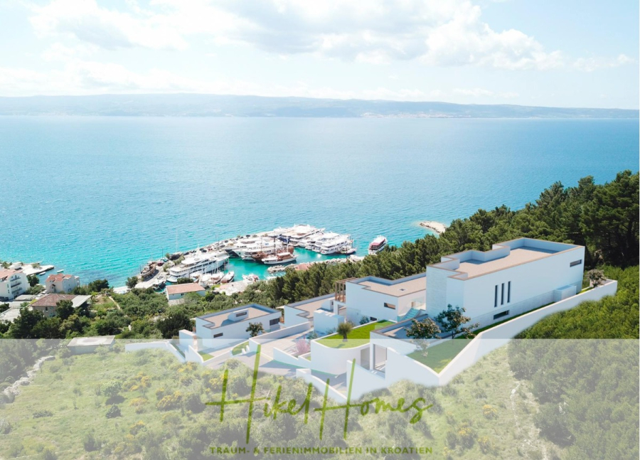 Villa Dalia – von jedem Zimmer aus Meerblick mit 4 Schlafzimmer / 4 Bädern / Loggia / Pool / … - Luftaufnahme von modernen weißen Villen, umgeben von Grün auf einem Hügel mit Blick auf einen Jachthafen mit Yachten und Booten, mit dem blauen Meer und der fernen Küstenlinie im Hintergrund. Der Text am unteren Rand lautet "Holz Homes". (46783)