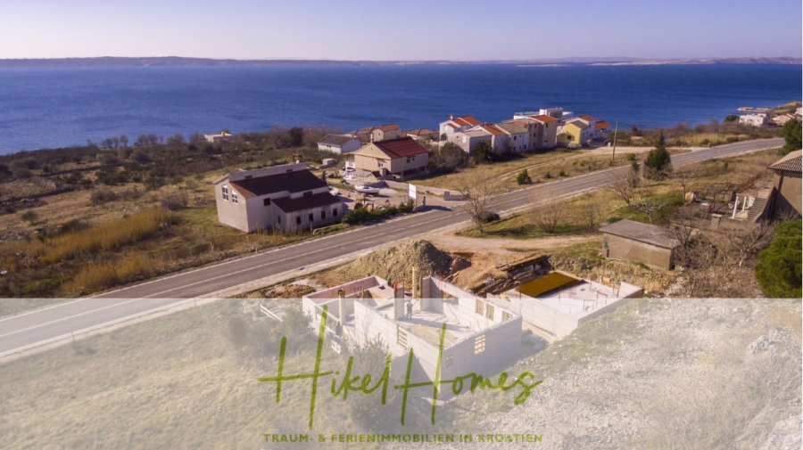 Neubau Meerblick 270m vom Meer entfernt – 3 SZ mit Bädern, Pool, Fertigstellung 2025 - Ein Küstendorf in Kroatien mit Häusern in der Nähe einer Straße, mit Blick auf ein ruhiges blaues Meer unter einem klaren Himmel. Im Vordergrund befindet sich eine Baustelle. Der überlagerte Text lautet: "Hikel Homes: Traum- & Ferienimmobilien in Kroatien. (44703)