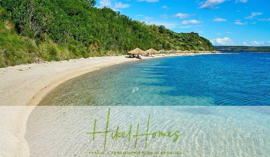 Neubau Meerblick 270m vom Meer entfernt – 3 SZ mit Bädern, Pool, Fertigstellung 2025 - Ein abgelegener Strand mit klarem, blauem Wasser, weißem Sand und grünem Gebüsch. Strohschirme und Liegestühle sind entlang des Ufers aufgereiht. Auf dem Bild ist der Text "Hikel Homes" zu lesen. (44697)