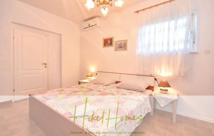 1. Reihe dirkt Meer mit 5 SZ, Pool, Jacuzzi, … auf der Insel Ciovo (bei Trogir mit 2 Brücken) - Ein helles Schlafzimmer mit einem Doppelbett, das mit einer bunten Patchworkdecke bedeckt ist. Zwei Nachttische mit Lampen, ein Fenster mit durchsichtigen Vorhängen und eine Klimaanlage sind zu sehen. Das Zimmer hat helle Wände und einen gefliesten Boden. (44926)