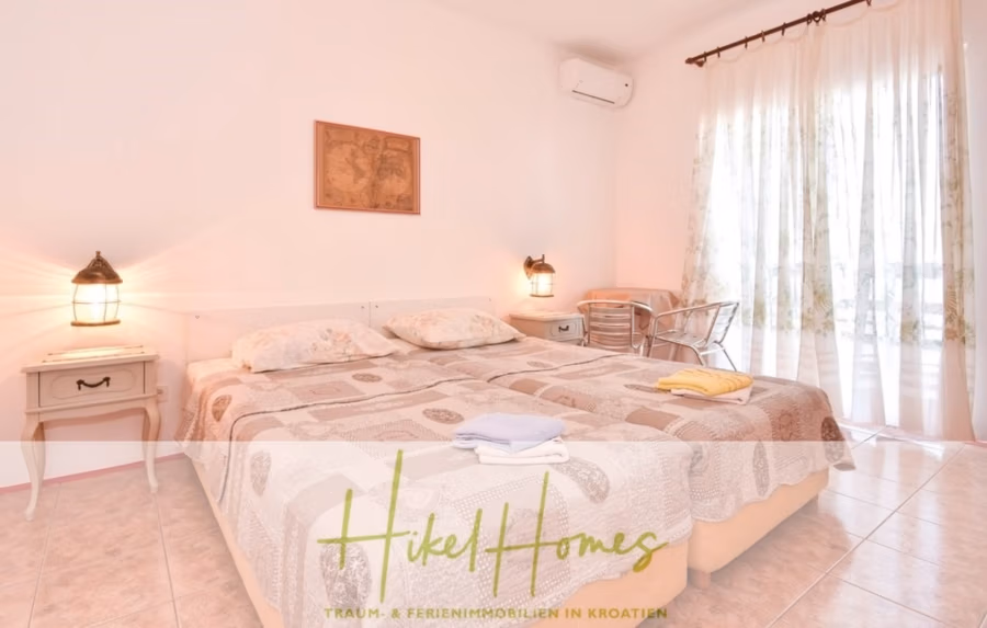 1. Reihe dirkt Meer mit 5 SZ, Pool, Jacuzzi, … auf der Insel Ciovo (bei Trogir mit 2 Brücken) - Ein gemütliches Schlafzimmer mit einem großen Bett und gemusterter Bettwäsche. Sanftes Licht von zwei Lampen auf Beistelltischen und einem Fenster mit transparenten Vorhängen. Ein kleines Tischset steht in der Nähe des Fensters, in einem Raum mit gefliestem Boden und sanften Farben. (42942)