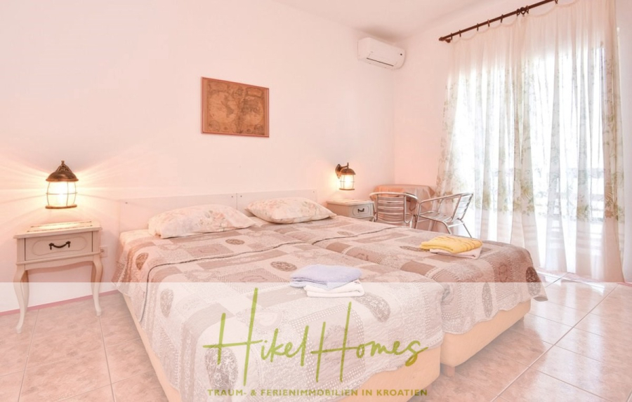 1. Reihe dirkt Meer mit 5 SZ, Pool, Jacuzzi, … auf der Insel Ciovo (bei Trogir mit 2 Brücken) - Ein helles, luftiges Schlafzimmer mit einem großen Bett, beige gemusterter Bettwäsche, zwei Nachttischen mit Lampen, einer Wandkarte, einem kleinen Schreibtisch mit einem Stuhl, Fliesenboden und durchsichtigen Vorhängen, die das natürliche Licht hereinlassen. (44931)