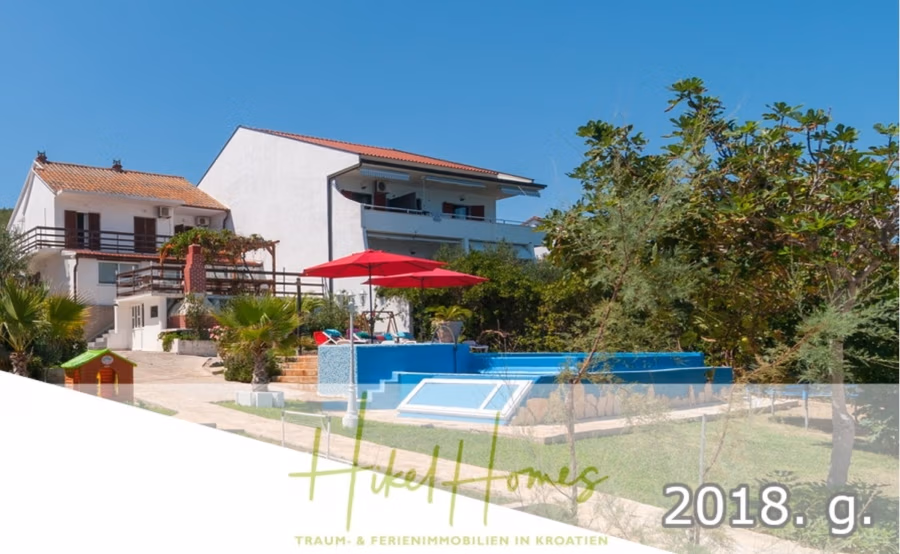1. Reihe dirkt Meer mit 5 SZ, Pool, Jacuzzi, … auf der Insel Ciovo (bei Trogir mit 2 Brücken) - Ein zweistöckiges Haus mit weißer Fassade und rotem Ziegeldach ist von Grünflächen und einem kleinen Pool umgeben. Ein roter Sonnenschirm spendet Schatten am Poolbereich. In der unteren rechten Ecke ist die Jahreszahl „2018“ vermerkt, und am unteren Rand befindet sich ein Markenzeichen. (42952)