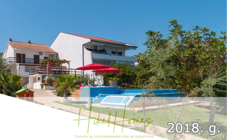 1. Reihe dirkt Meer mit 5 SZ, Pool, Jacuzzi, … auf der Insel Ciovo (bei Trogir mit 2 Brücken) - Ein modernes weißes Ferienhaus mit Balkonen, einem kleinen blauen Pool, einem roten Sonnenschirm, Palmen und grünem Rasen unter einem klaren blauen Himmel. Der Text lautet "Huse Homes" und "2018. g." im Vordergrund. (44942)