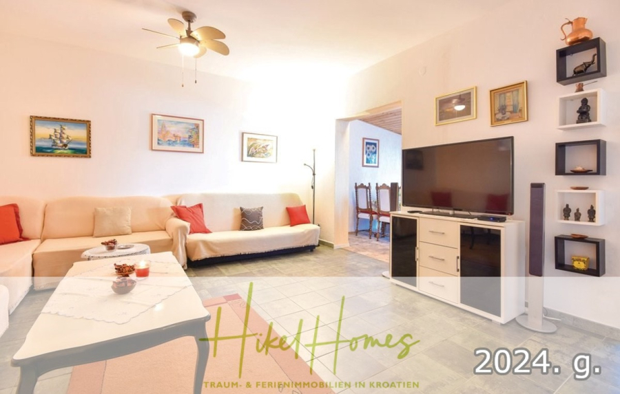 1. Reihe dirkt Meer mit 5 SZ, Pool, Jacuzzi, … auf der Insel Ciovo (bei Trogir mit 2 Brücken) - Helles Wohnzimmer mit beigen und roten Sofas, einem großen Flachbildfernseher auf einem weißen Ständer, Couchtischen und Wandkunst. Der Raum geht in einen Essbereich über. Textüberlagerung liest "Hiked Homes" und "2024. g. (44927)