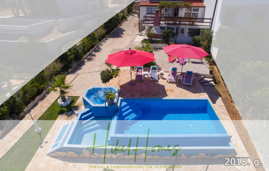 1. Reihe dirkt Meer mit 5 SZ, Pool, Jacuzzi, … auf der Insel Ciovo (bei Trogir mit 2 Brücken) - Luftaufnahme eines Swimmingpools mit blauen Fliesen, umgeben von Liegestühlen und roten Sonnenschirmen. In der Nähe befinden sich ein Whirlpool und ein weißes Gebäude mit Balkonen. Grünpflanzen säumen die Steinterrasse. Der Text ist am unteren Rand eingeblendet. (44939)