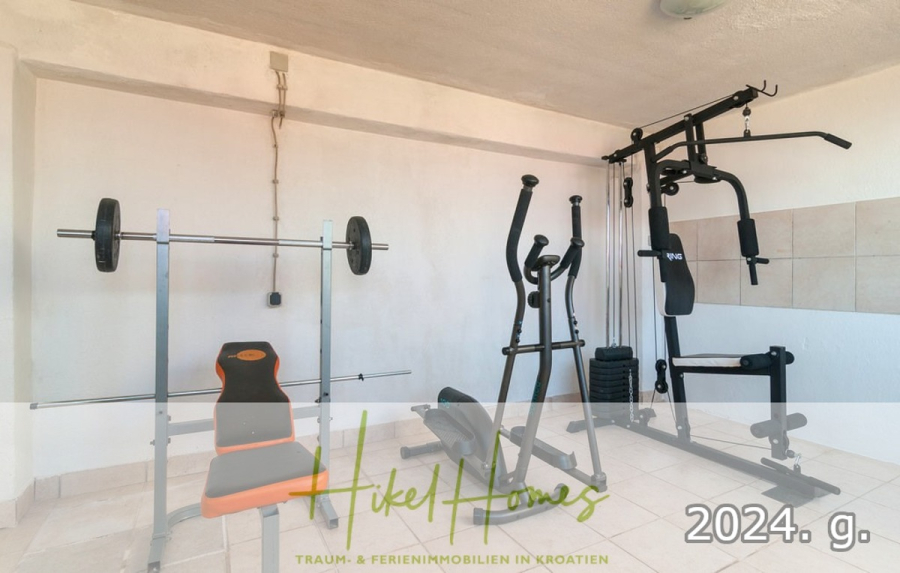 1. Reihe dirkt Meer mit 5 SZ, Pool, Jacuzzi, … auf der Insel Ciovo (bei Trogir mit 2 Brücken) - Ein kleiner Fitnessraum mit einer Hantelbank, einer Langhantel, einem Ellipsentrainer und einer Multigym-Station. Der Raum hat weiße Wände und geflieste Böden. Auf dem Text darüber steht "Hikel Homes" und "2024. g." am unteren Rand. (44934)