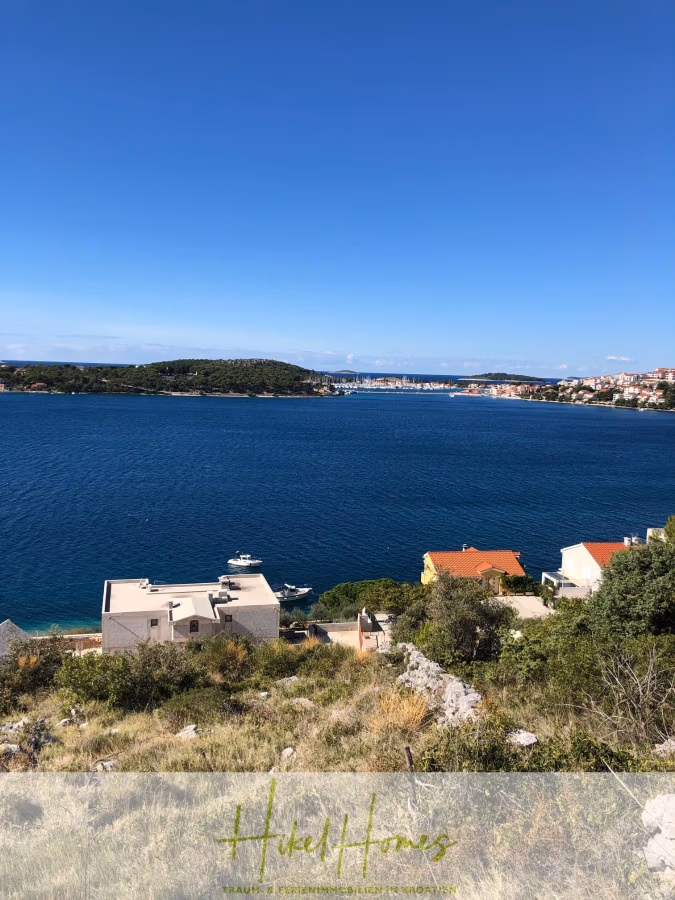 Luxus Villa Zlato – sehr ruhige Wohngegend – eigener Meerzugang, Boje, Pool, Lift und 391m² WFL - Küstenansicht mit blauem Meer und Himmel, übersät mit weißen und roten Dächern, Häusern und Booten. Im Hintergrund sind eine Brücke und weiteres Land zu sehen. Im Vordergrund sind grüne Sträucher und ein Hügel zu sehen. (41812)