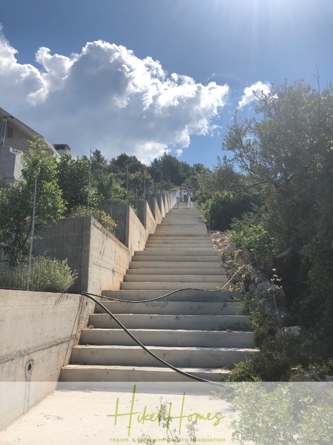 Luxus Villa Zlato – sehr ruhige Wohngegend – eigener Meerzugang, Boje, Pool, Lift und 391m² WFL - Eine lange, steile Treppe aus Beton führt zwischen grünen Sträuchern und Bäumen unter einem sonnigen, wolkenverhangenen Himmel nach oben. Oben sind ein paar Menschen zu sehen. Ein Gartenschlauch liegt entlang der Treppe. (45086)