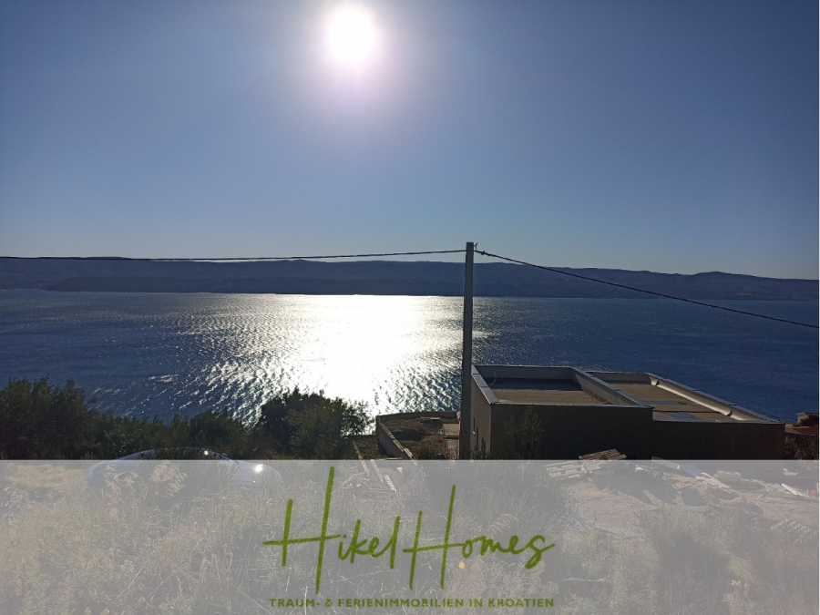 1515m² Bauland mit fertigen Bauprojekt in Panoramahanglage mit traumhaften Rundumblick aufs Meer - Eine strahlende Sonne scheint über einem ruhigen Meer mit schimmernden Reflexen, betrachtet von einem Hügel mit einigen Grünflächen und Dächern unterhalb. Der Text "Hikel Homes Traum- & Ferienimmobilien in Kroatien" ist am unteren Rand eingeblendet. (46744)