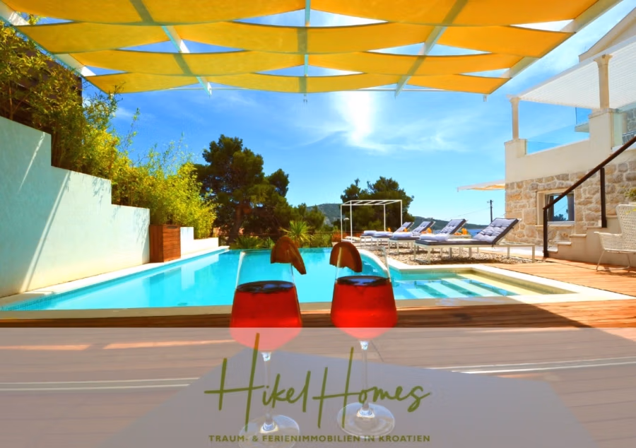 Sehr großzügige Meerblick Villa mit 300m² auf 800m² Grundstück, 4 Garagen, Pool, Terrassen - Zwei Gläser roten Safts mit Fruchtgarnitur stehen auf einem Tisch mit Blick auf den Pool. Gelbe Farbtöne hüllen den Bereich mit Liegestühlen am Poolrand, umgeben von Grün. Sonniger, klarer Tag mit blauem Himmel. (43265)