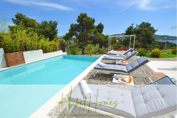 Moderner Poolbereich mit gepolsterten Liegestühlen, kleinen Tischen mit Getränken und Obst und üppiger Bepflanzung. Der türkisfarbene Pool blickt auf eine malerische Landschaft mit Hügeln und Bäumen unter einem klaren blauen Himmel. - Sehr großzügige Meerblick Villa mit 300m² auf 800m² Grundstück, 4 Garagen, Pool, Terrassen