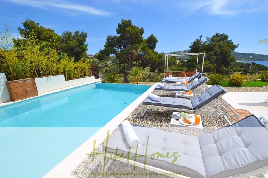 Sehr großzügige Meerblick Villa mit 300m² auf 800m² Grundstück, 4 Garagen, Pool, Terrassen - Ein luxuriöser Außenpoolbereich mit mehreren Liegestühlen und Beistelltischen. Vom Pool aus bietet sich ein malerischer Blick auf Grünflächen und Hügel unter einem strahlend blauen Himmel. Auf den Tischen stehen Obstteller und Getränke bereit. (43264)
