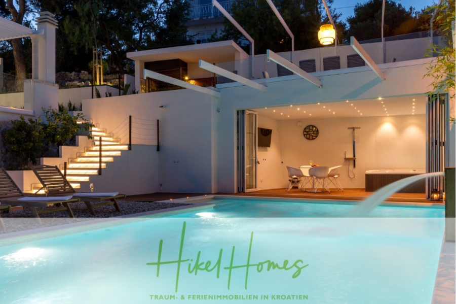 Sehr großzügige Meerblick Villa mit 300m² auf 800m² Grundstück, 4 Garagen, Pool, Terrassen - Moderne Villa in der Abenddämmerung mit beleuchtetem Pool, Sonnenliegen und offener Terrasse, die einen Essbereich und einen Whirlpool bietet. Eine Außentreppe mit Beleuchtung führt zu einer oberen Terrasse. Das "Hikel Homes"-Logo ist am unteren Rand eingeblendet. (44902)