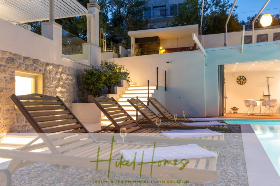 Sehr großzügige Meerblick Villa mit 300m² auf 800m² Grundstück, 4 Garagen, Pool, Terrassen - Moderner Außenpoolbereich in der Abenddämmerung mit mehreren Holzliegen, Handtüchern und Weingläsern neben einem leuchtenden Pool. Eine Treppe führt hinauf zu einem modernen Haus mit beleuchteten Terrassen und großen Glastüren. (44905)