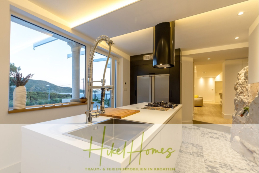 Sehr großzügige Meerblick Villa mit 300m² auf 800m² Grundstück, 4 Garagen, Pool, Terrassen - Moderne Küche mit großer Inselspüle, Gasherd, Edelstahlgeräten und Panoramafenstern mit Blick auf die malerische Hügellandschaft. Der Text am unteren Rand lautet "Hikel Homes - Traum- & Ferienimmobilien in Kroatien. (44889)