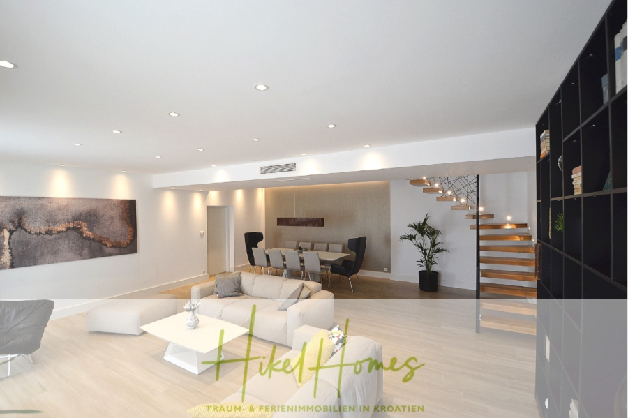 Sehr großzügige Meerblick Villa mit 300m² auf 800m² Grundstück, 4 Garagen, Pool, Terrassen - Moderner offener Wohn- und Essbereich mit hellen Holzböden, neutralen Möbeln, Wandkunst, schwarzen Regalen und einer Schwebetreppe mit Holzstufen, die nach oben führt. (44885)