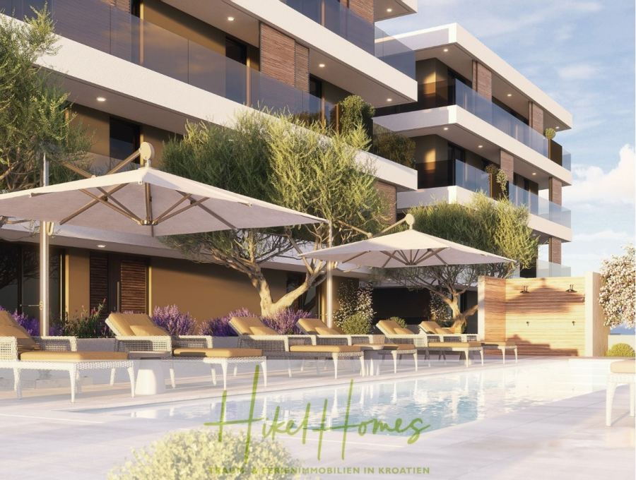 1. Reihe Luxus Neubau Penthouse – Meerblick mit 3 SZ, riesige Terrasse und Gemeinschaftspool (S6A) - Ein modernes Apartmentgebäude mit Balkonen bietet an einem sonnigen Tag einen Blick auf einen Poolbereich mit Liegestühlen, großen Sonnenschirmen, Bäumen und einem klaren Schwimmbecken. Der Schriftzug "Hikel Homes" ist am unteren Rand sichtbar. (46210)
