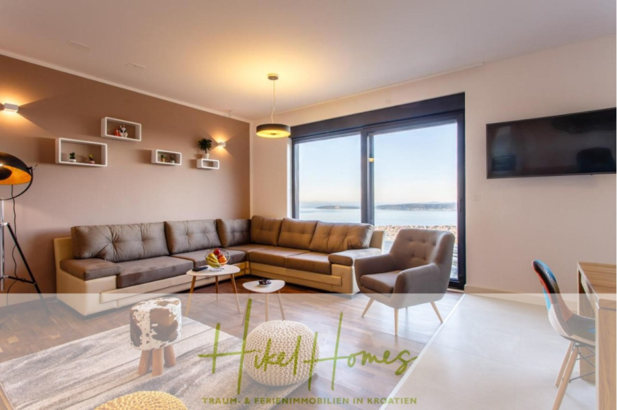 Meerblick auf 2903m² großem Grundstück in wunderbarer Alleinlage am Stadtrand von Split - Ein modernes Wohnzimmer mit einem großen grauen Sektionssofa, einem kleinen runden Couchtisch, an der Wand befestigten Regalen, einem Flachbildfernseher und großen Fenstern, die einen malerischen Meerblick bieten. Der Raum ist hell und stilvoll eingerichtet. (45839)